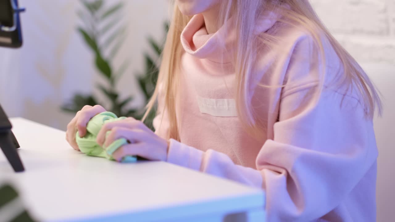 маленькая девушка-блоггер-инфлюенсер разговаривает с подписчиками в прямом эфире, играет с зеленой слизью. модная жидкая игрушка, растягивающаяся в сторону. ребёнок смотрит на экран смартфона дома.