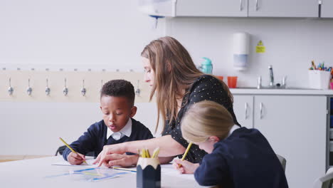 Female-school-teacher-sitting-with-two-primary-school-kids,-helping-a-boy-with-his-work,-close-up