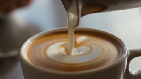 pouring latte art with a heart design into a coffee cup