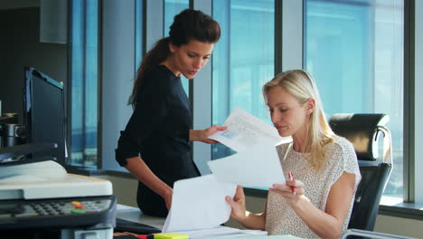 two businesswomen working at desk discuss document