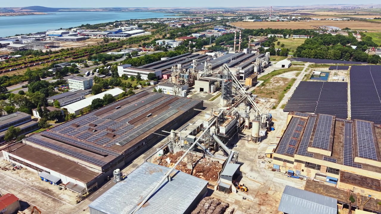 Gündüz bir nehrin yakınında, makine ve yapıları gösteren, fabrikalar ve güneş panelleri bulunan büyük bir sanayi sitesi