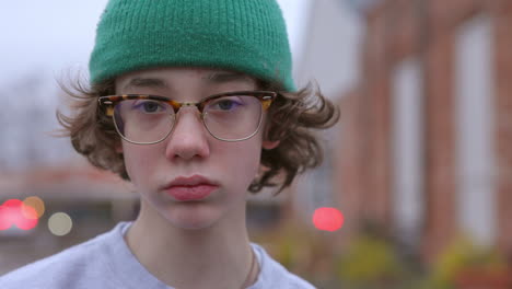 teen boy outside in a green hat and glasses looks at camera