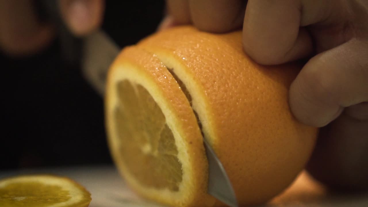 primer plano de un cuchillo afilado cortando y rebanando una naranja jugosa en cámara lenta