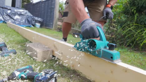 a wide shot of plank of wood being planed in a garden by a man on a sunny day in 4 x slow motion