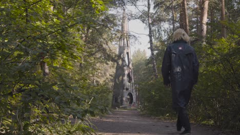 person walking through forest path near an abstract concrete sculpture