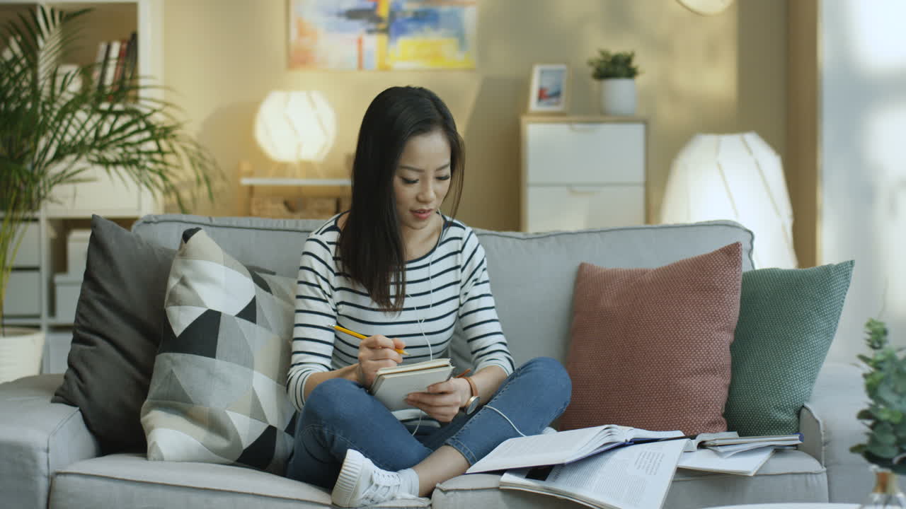 Young Woman In Striped Shirt And Wearing Headphone Studying With Textbooks And Taking Notes On Notebook 1