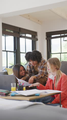 vertical video of happy diverse teenager girls using laptop at home, slow motion