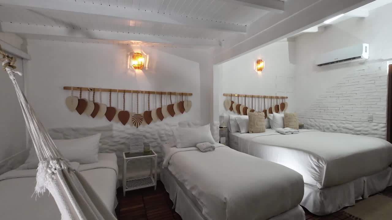 Minimalist white bedroom with two single beds, one double bed and a hammock in a tropical-caribbean style interior perfect for family vacation stays
