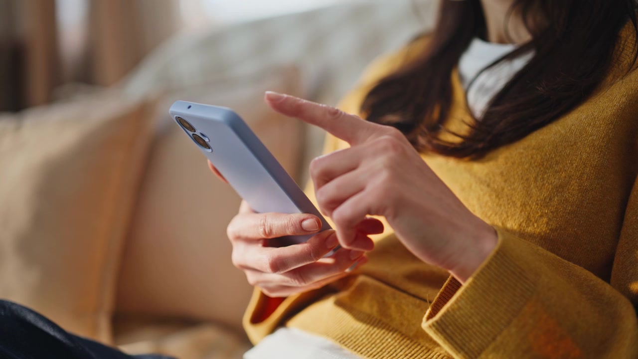 Dita di donna che scorrono lo schermo del cellulare scegliendo acquisti online a casa, primo piano