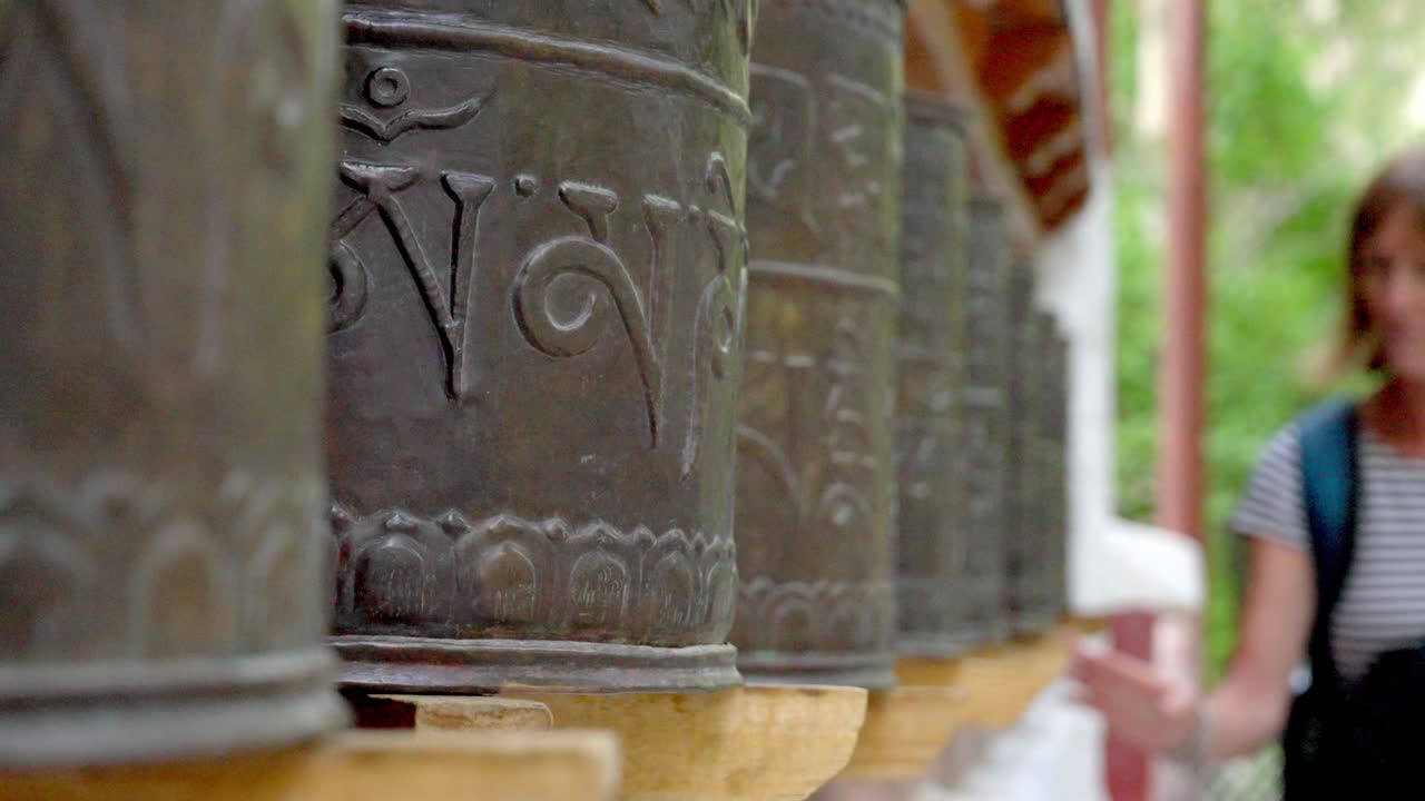A serene shot of Buddhist prayer wheels in Alchi Monastery, Ladakh, with an older tourist in soft focus slow motion moves large religious wheels. Religious journey self discovery for older traveller.