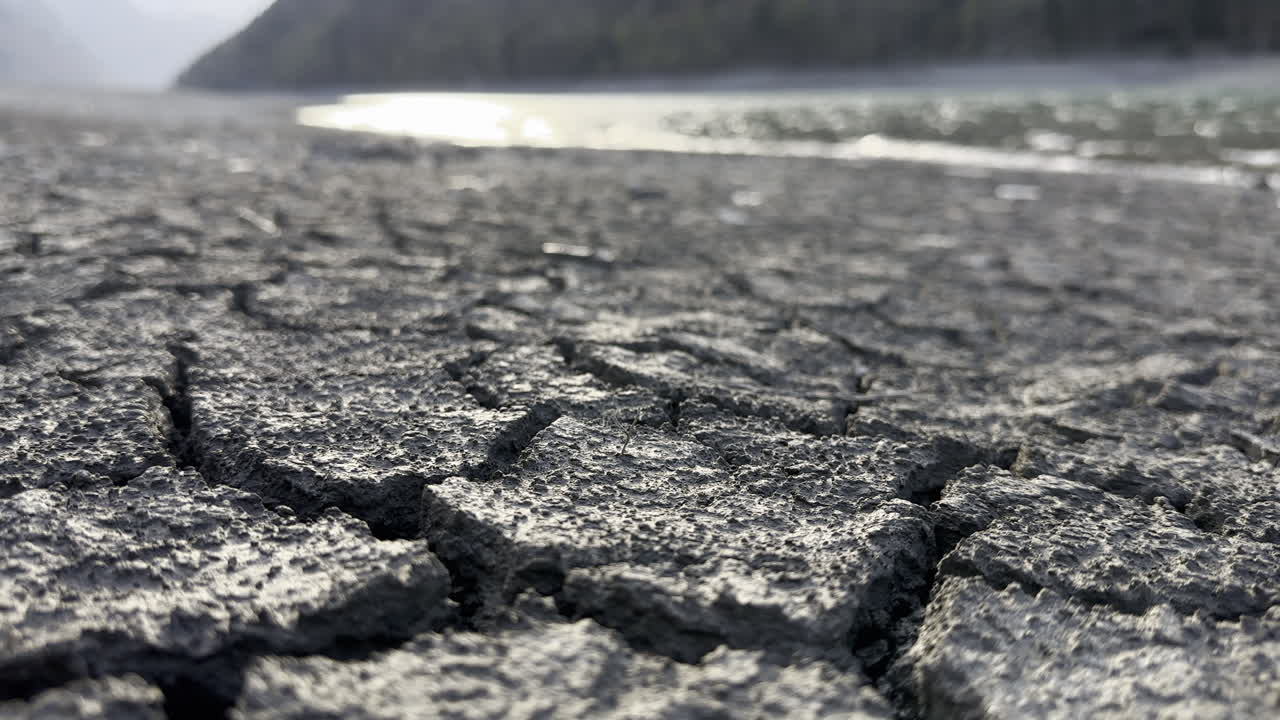 Inquadratura dal basso del terreno crepato che contrasta con l'acqua abbondante sulle rive del lago Klöntalersee, Cantone di Glarona, Svizzera.