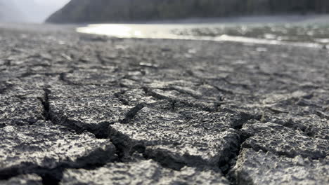 Low-shot-of-The-cracked-ground-contrasts-with-the-abundant-water-on-the-shores-of-the-Klöntalersee-lake,-Glarus-Kanton,-Switzerland