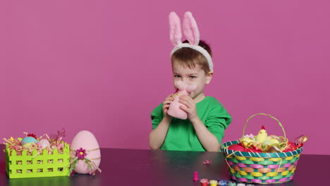 adorable little child playing with a stuffed rabbit and a pink egg at table