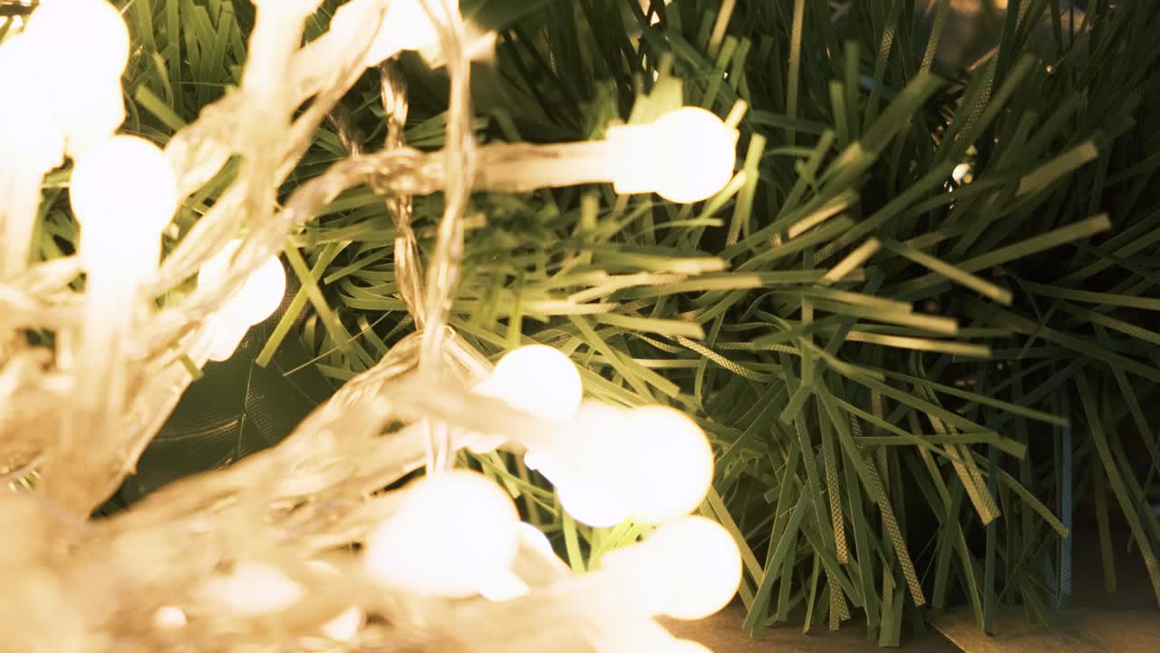 Latar belakang Tahun Baru atau Natal. Close-up cabang cemara buatan yang dihiasi dengan bola Natal merah dan lampu hias berkedip.