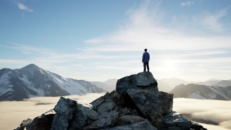 adventurous male hiker standing on dramatic rocky cliff, low clouds and snowy mountain landscape