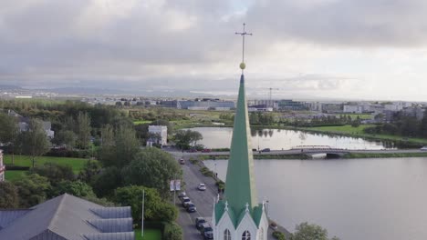 cruz en la torre puntiaguda de la iglesia libre en reykjavik, islandia, lago tjörnin