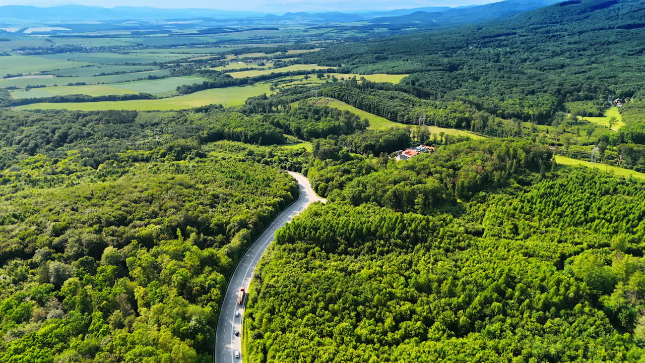 Winding road in green landscape. A winding road cuts through expansive green forests under a clear blue sky, showcasing nature's beauty on a sunny day