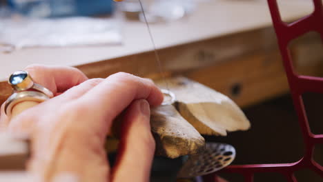 close up of female jeweller working on ring with saw in studio