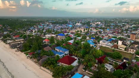 Experience-Paje,-Zanzibar-at-sunset:-drone-captures-beach,-cityscape,-palm-trees,-and-vibrant-blue-sky