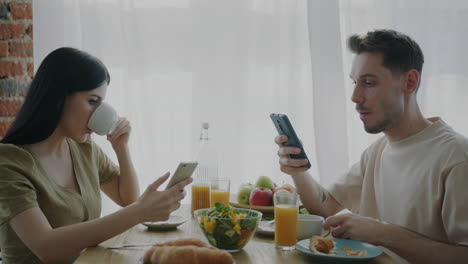 couple having breakfast while looking at their phones