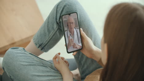 woman checks possible symptoms with professional physician using online video chat. young girl sick at home using smartphone to talk to her doctor via video conference medical app.