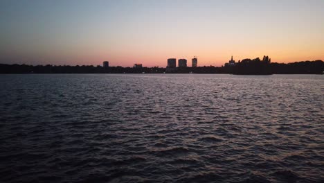 Olas-En-El-Lago-Herastrau,-Bucarest-Al-Atardecer-Con-Edificios-Distantes-En-El-Fondo