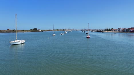 drone shot flying low over the water surface with sailboats anchored on either side