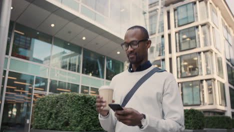 african american businessman walking through city using smart phone