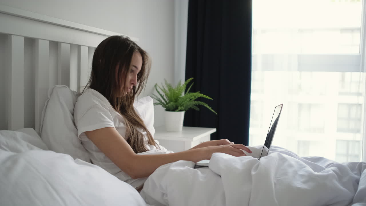 침대에 노트북으로 일하는 여자