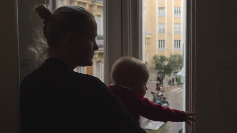 adorable baby girl looking out the window with her mother