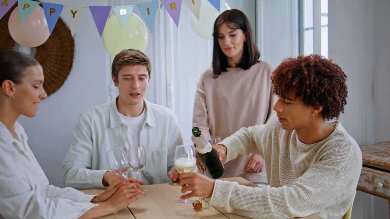 Festive man pouring champagne bottle at kitchen closeup. Friends pouring drink