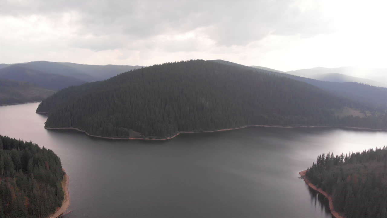Aerial Footage of Large Lake and mountains surrounded by Pine Forest trees