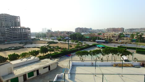 Aerial-tilting-up-view-of-a-highway-of-the-city-with-traffic-going-on,-under-constructed-building,-a-sports-area-and-empty-plot-with-its-roads