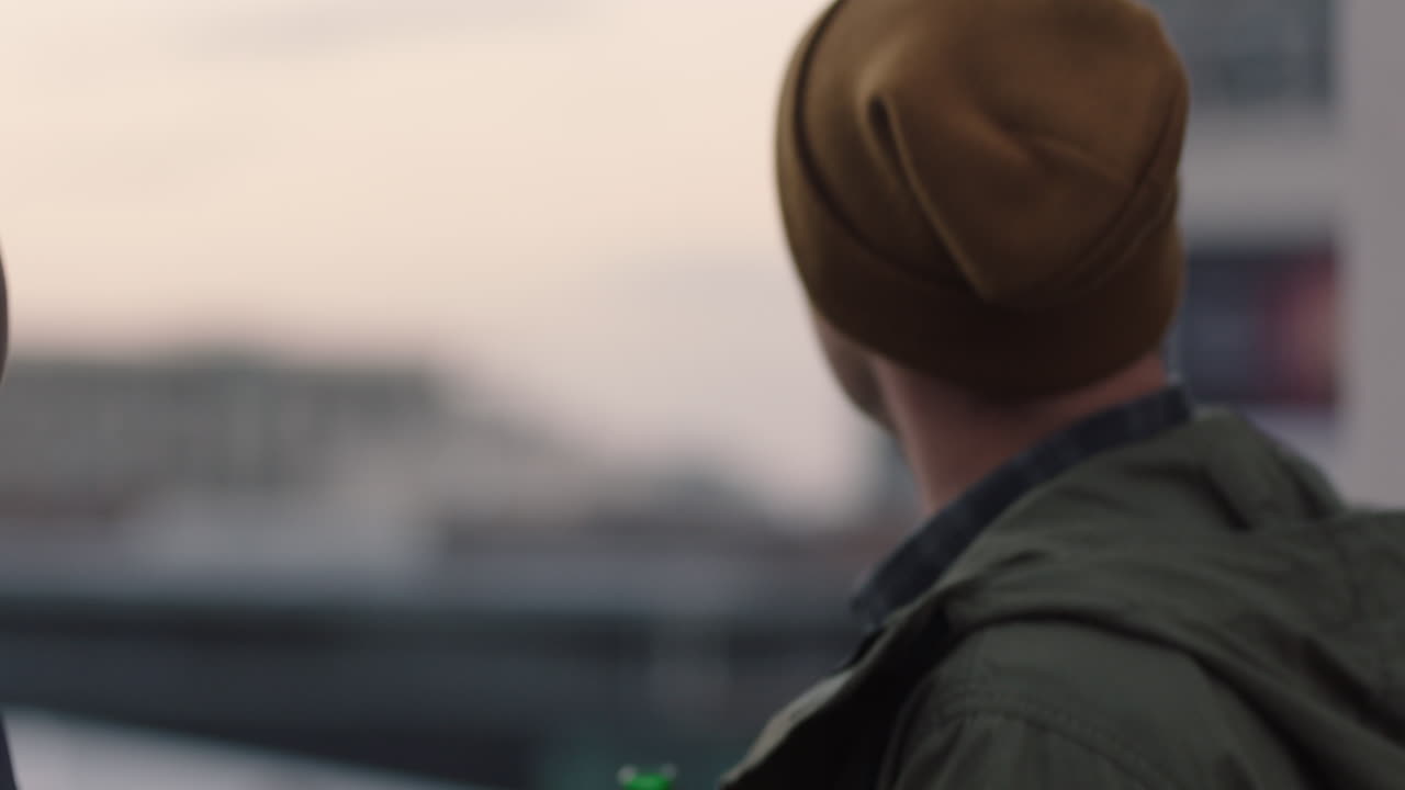 행복한 친구들이 옥상에서 포옹하고 우정을 즐기고 재결합하고 술을 마시며 대화를 나누며 해가 지는 도시의 전망을 공유합니다.