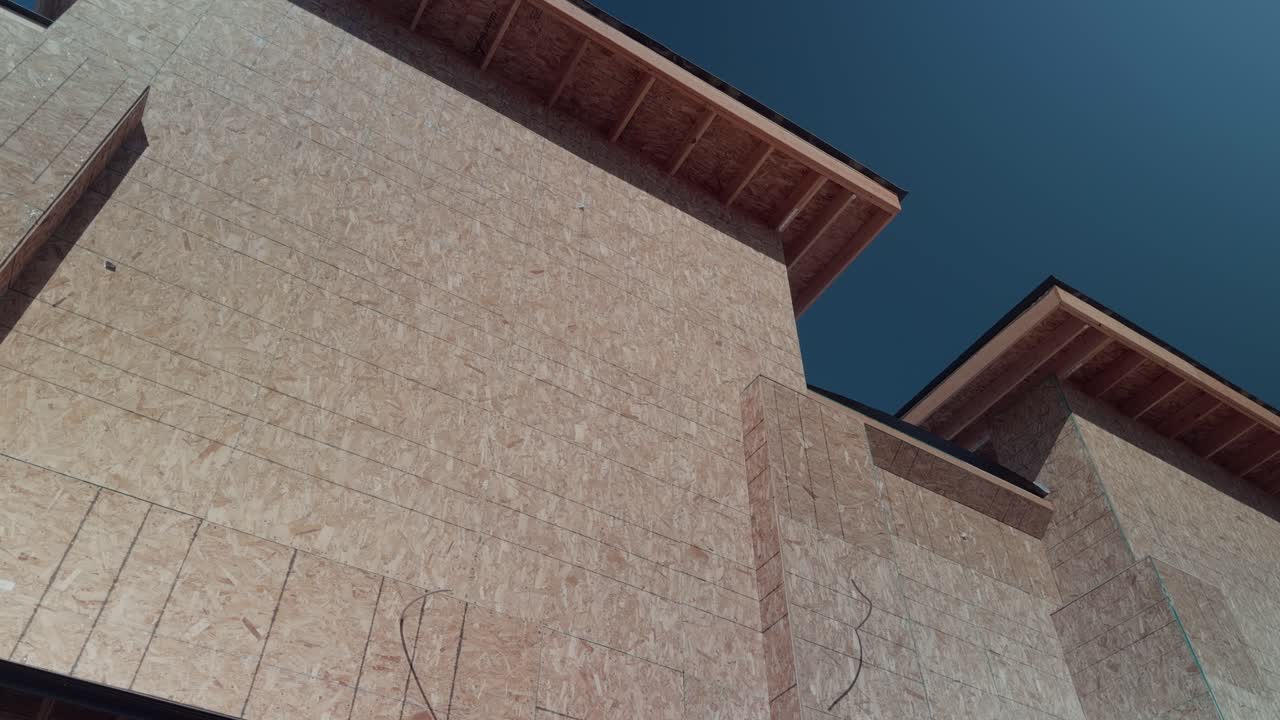 Panorâmica ascendente constante de uma casa nova com estrutura de compensado sob um céu azul brilhante.