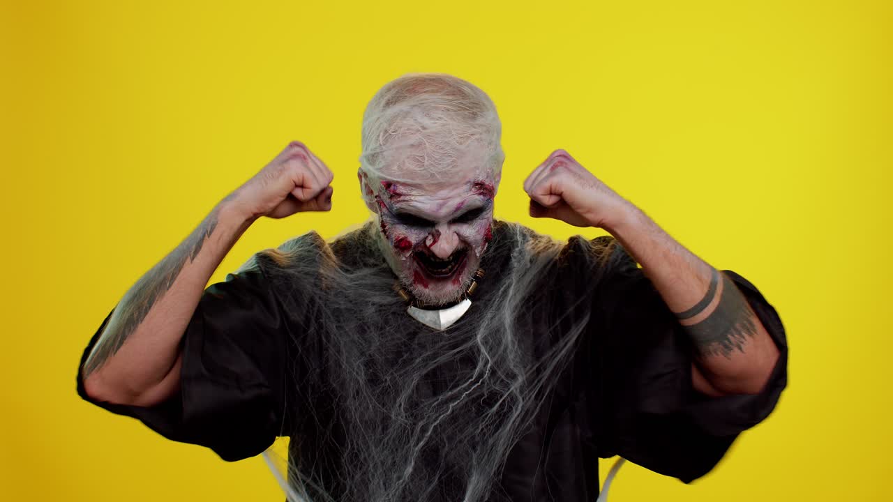 zombie aterrador halloween hombre celebrar el éxito ganar grito se regocija haciendo ganador manos gesto decir sí