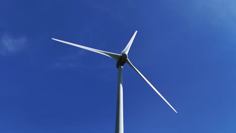 Wind-turbine-spinning-against-a-clear-blue-sky,-captured-from-a-low-angle