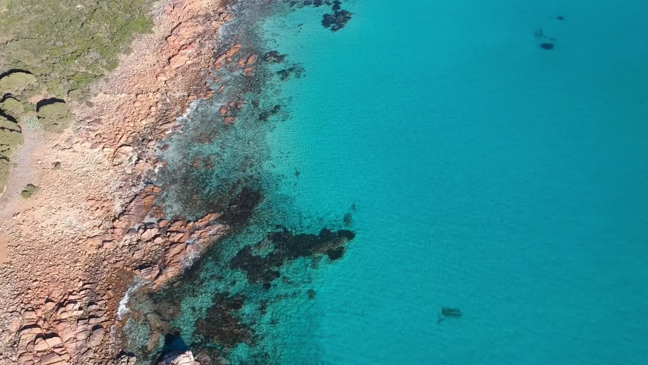drone aéreo de arriba hacia abajo moviéndose hacia el océano con aguas cristalinas y tranquilas de color turquesa en castle rock, australia occidental