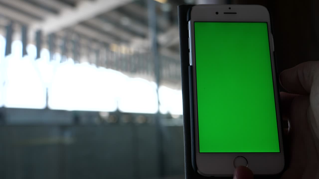 공공 기차역에서 손에 녹색 스크린 휴대전화를 들고 있습니다.