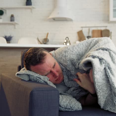man feeling sick on the couch at home with cold and flu symptoms. pandemic
