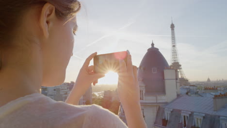 happy woman using smartphone taking photo enjoying sharing summer vacation experience in paris photographing beautiful sunset view of eiffel tower on balcony close up