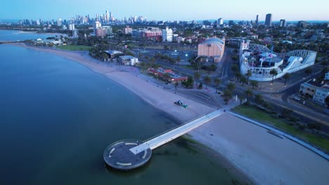 St-Kilda-Beach,-luna-park-sand-rake-working-sunrise,-aerial-Australia