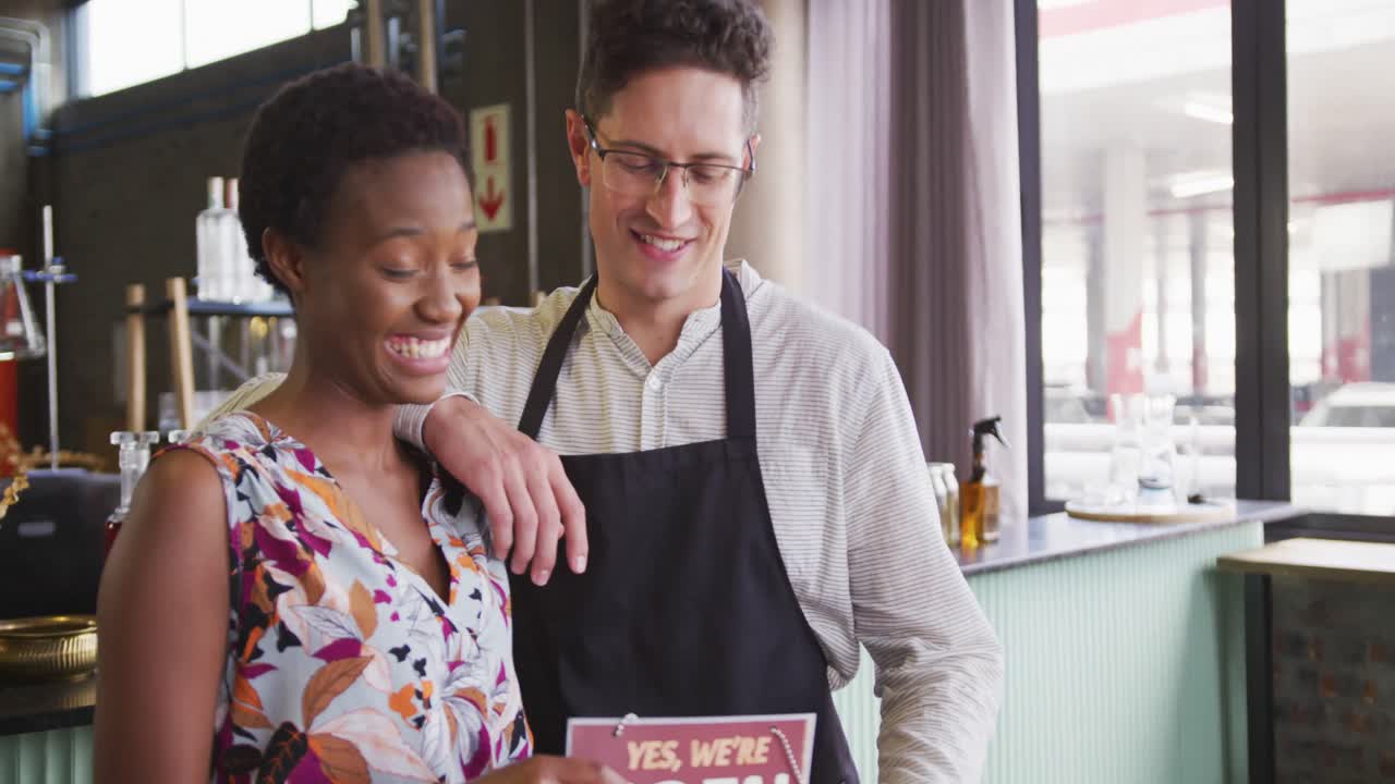 retrato de una feliz pareja diversa trabajando en una cafetería, de pie junto a la barra y sonriendo a la cámara