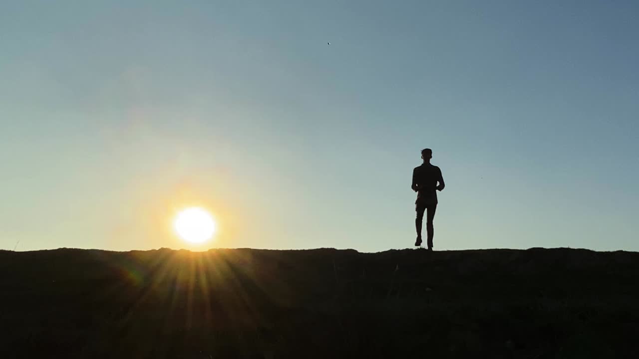 Silhouetted young man jogging on the spot against sunset