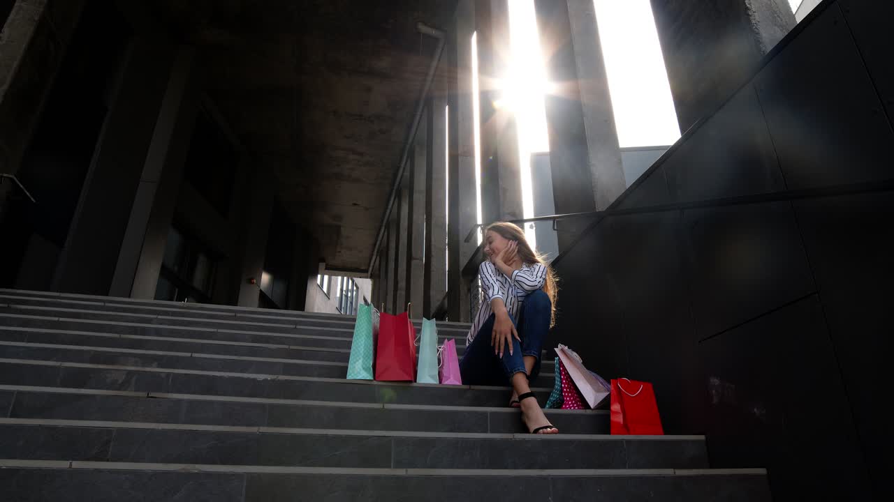 adolescente sonriente con bolsas de compras sentada en las escaleras cerca del centro comercial. venta de viernes negro