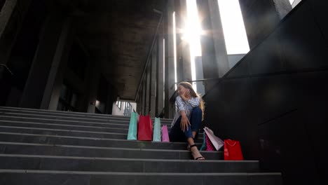 Teenager-smiling-girl-with-shopping-bags-sitting-on-stairs-near-shopping-mall.-Black-Friday-sale