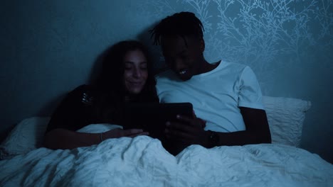 couple sitting up in bed watching something on their tablet device late at night