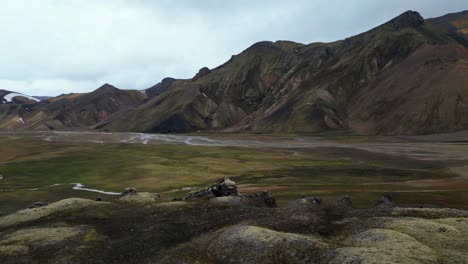 Incredible-mountains-and-river-aerial-views-of-Landmannalaugar-in-the-Highlands-of-Iceland-during-summer,-contrasting-with-lava-fields-and-different-shades-of-green-and-yellow