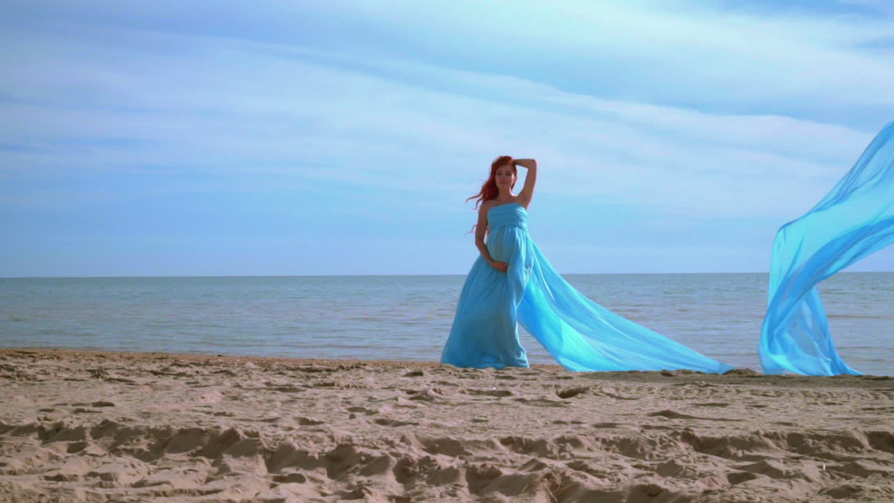 해변에서 포즈를 취하는 파란 드레스를 입은 임신한 여성. 해변 휴가.  ⁇ 만적인 여성