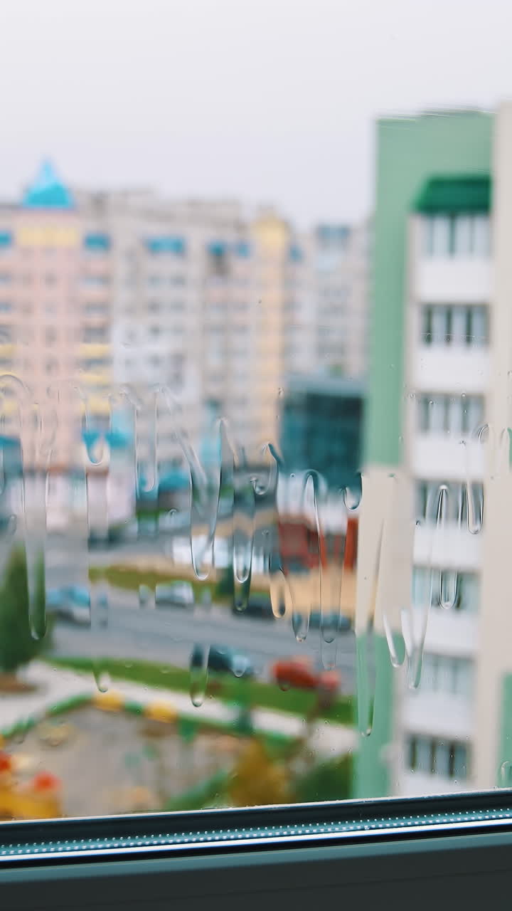 Cleaning window in the city. Man holding household brush and cleans window from outside. View from indoors. Urban buildings background. Vertical video